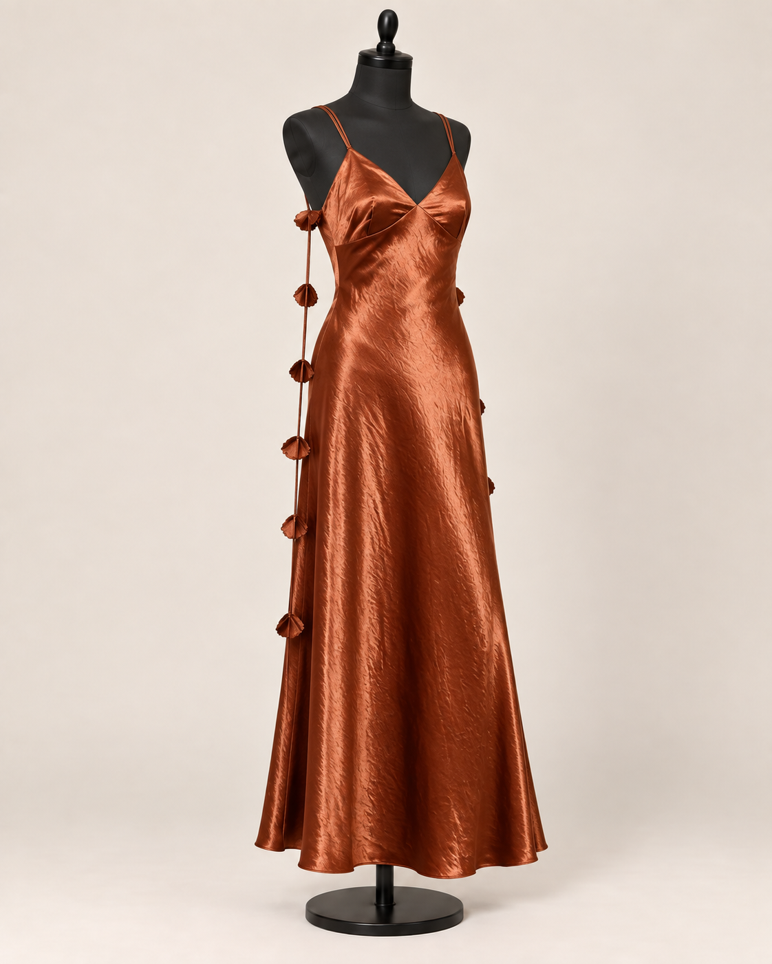 Copper-brown satin maxi dress with thin straps and floral cords on a black female dress form against a beige background